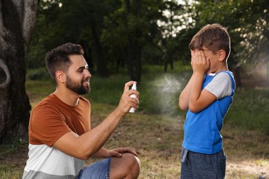 Photo of Man applying insect repellent on his son in park. Tick bites prevention