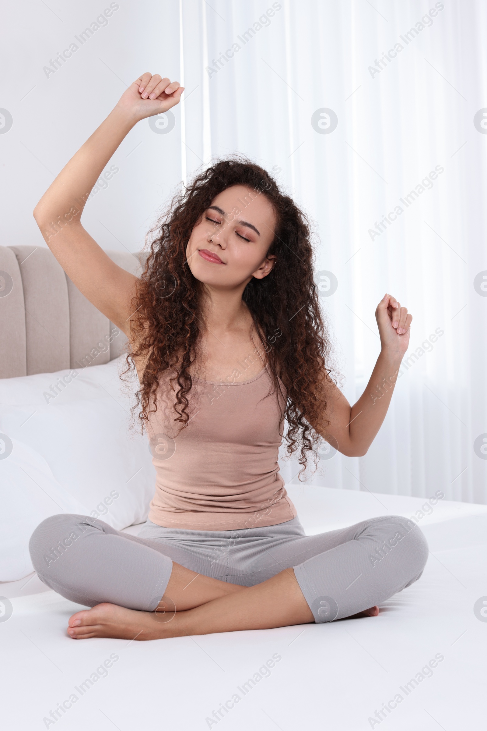 Photo of Happy African American woman stretching on bed at home
