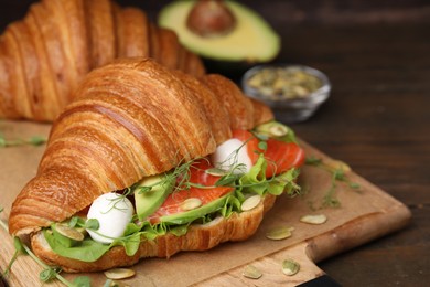 Tasty croissant with salmon, avocado, mozzarella and lettuce on wooden table, closeup