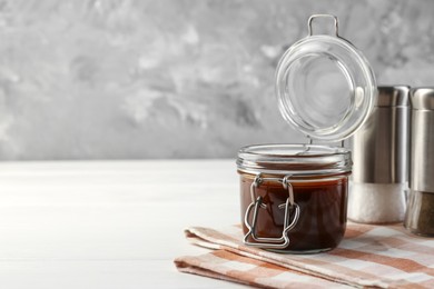 Photo of Tasty barbecue sauce in glass jar on white wooden table, space for text