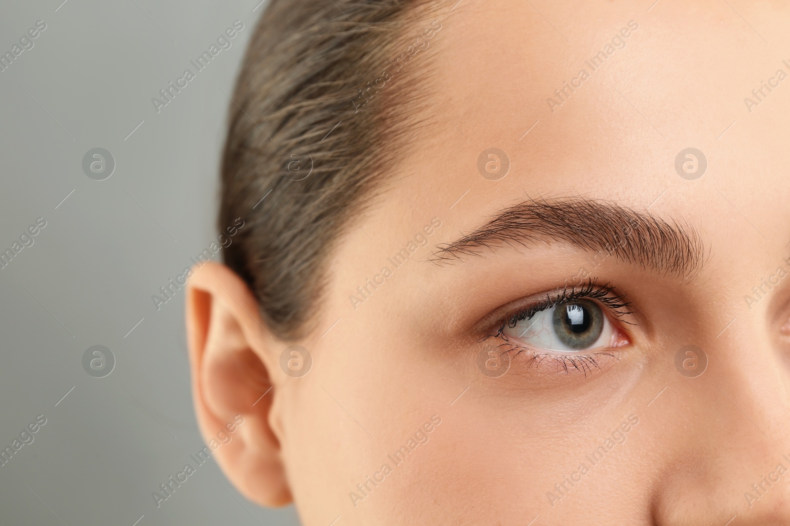 Photo of Young woman with perfect eyebrows on grey background, closeup. Space for text