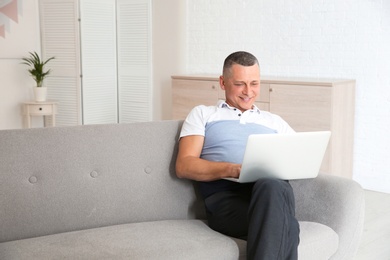 Photo of Mature man with laptop sitting on sofa at home