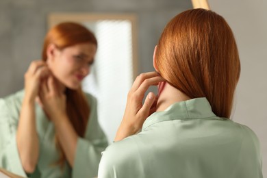Photo of Suffering from allergy. Young woman scratching her neck near mirror indoors, back view. Space for text