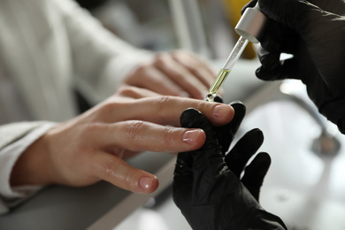 Photo of Professional manicurist pouring oil on client's nails in beauty salon, closeup