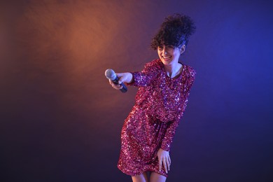 Photo of Beautiful young woman with microphone on color background in neon lights