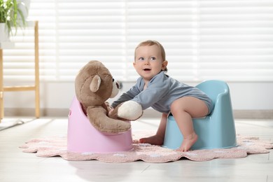 Photo of Little child and teddy bear sitting on plastic baby potties indoors