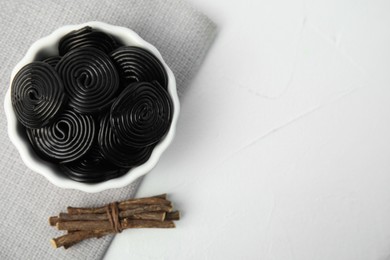 Tasty black candies and dried sticks of liquorice root on white table, flat lay. Space for text