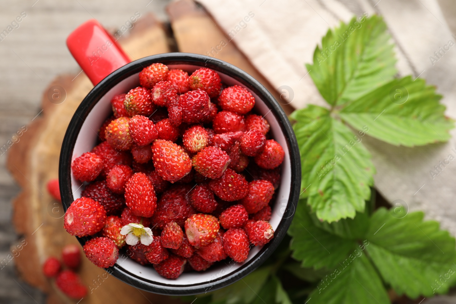 Photo of Fresh wild strawberries in mug and leaves on table, flat lay