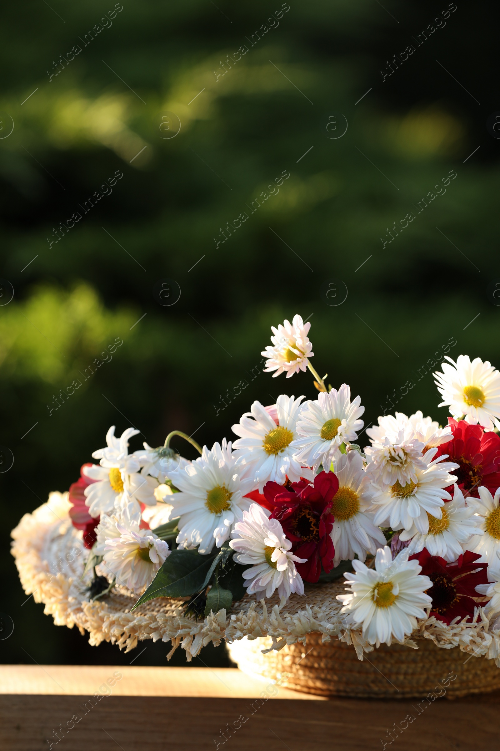 Photo of Beautiful wild flowers in wicker basket on wooden table against blurred background. Space for text