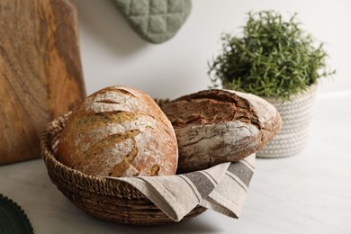 Photo of Wicker bread basket with freshly baked loaves on white marble table in kitchen