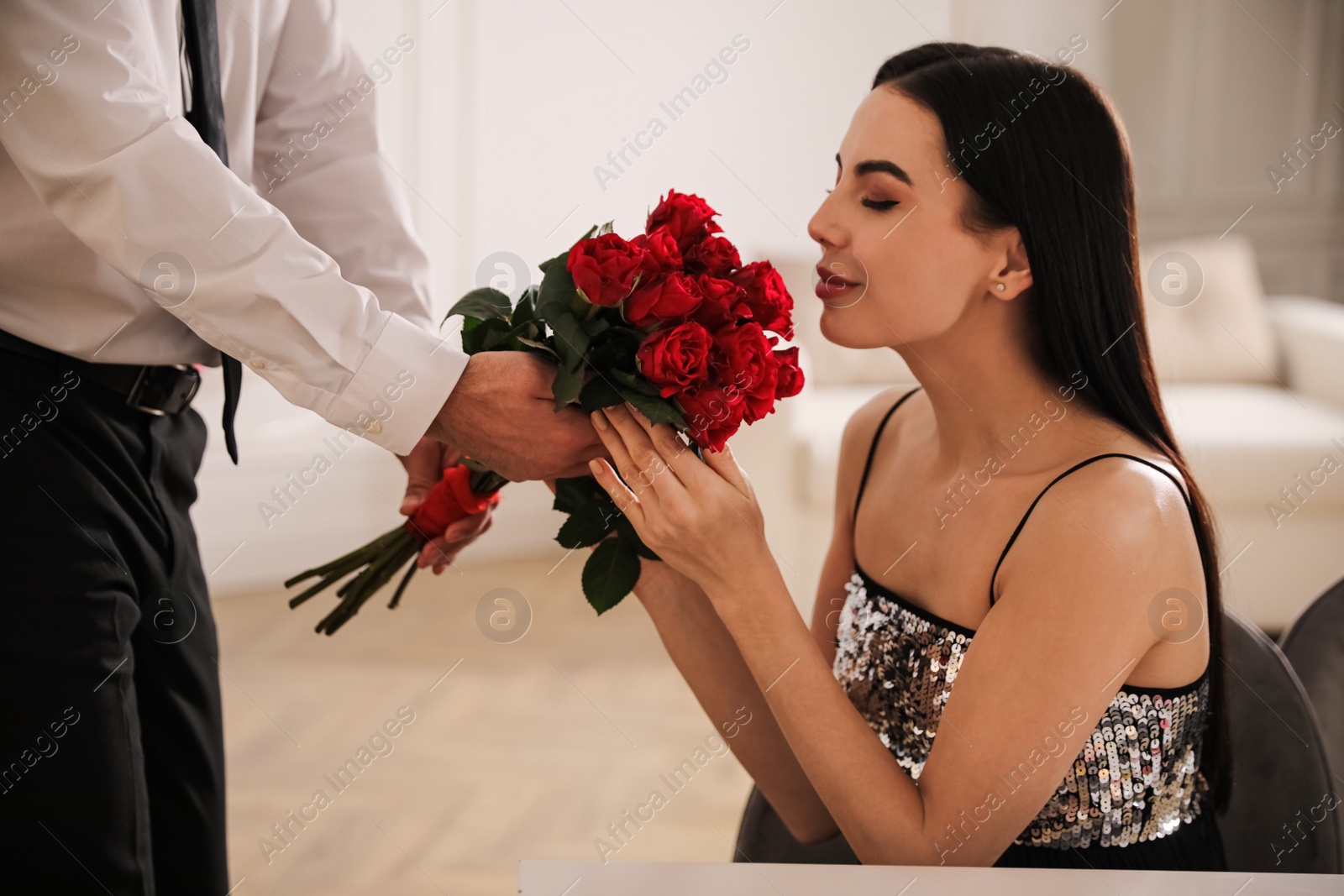 Photo of Man presenting roses to his beloved woman indoors. Valentine's day celebration