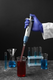 Photo of Laboratory analysis. Scientist dripping sample with micropipette into beaker at grey table, closeup