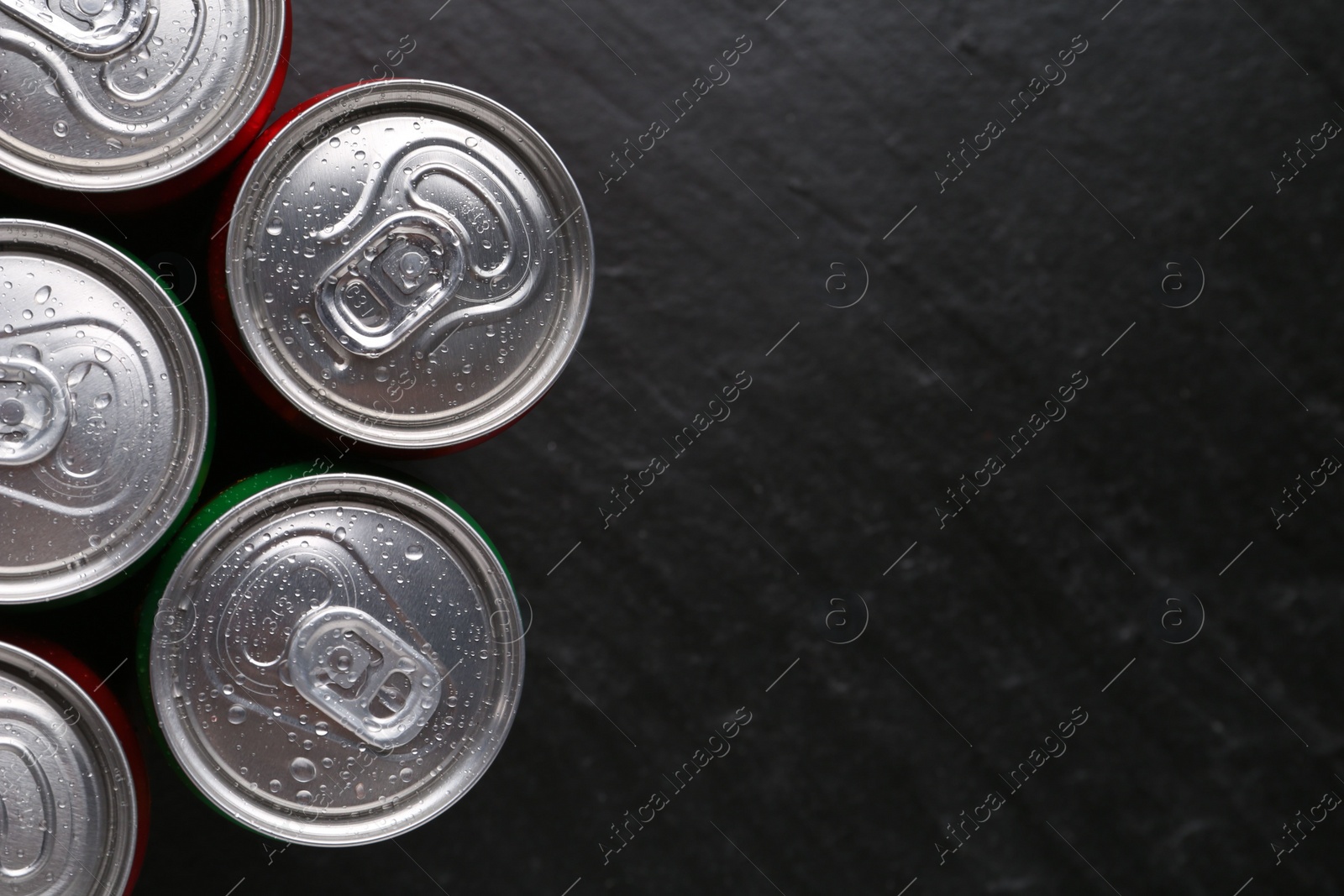 Photo of Energy drink in wet cans on black textured background, top view. Space for text