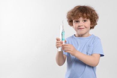 Cute little boy holding electric toothbrush and tube of toothpaste on white background, space for text