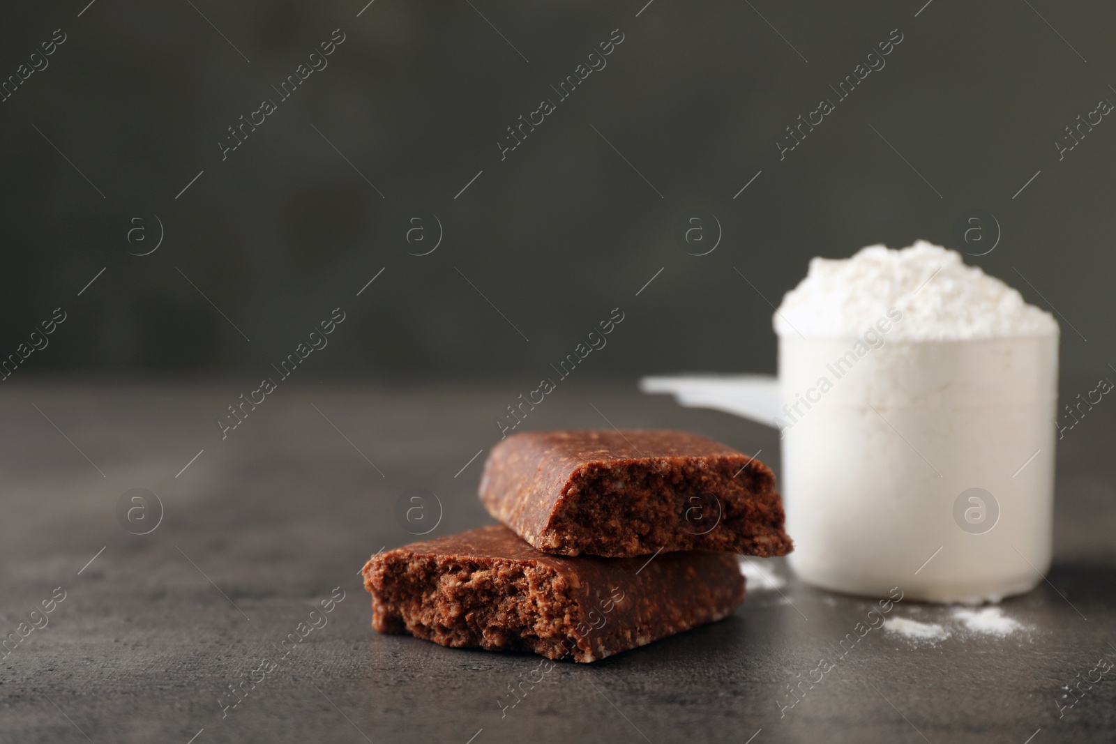 Photo of Tasty protein bar and scoop of powder on grey table. Space for text