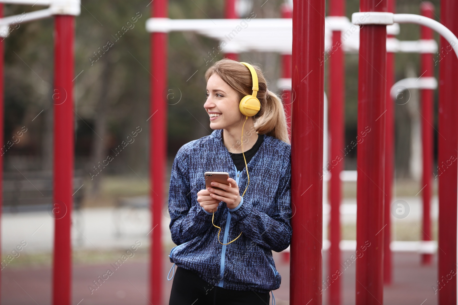 Photo of Young woman with headphones listening to music on sports ground