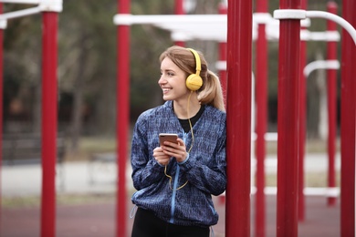 Photo of Young woman with headphones listening to music on sports ground