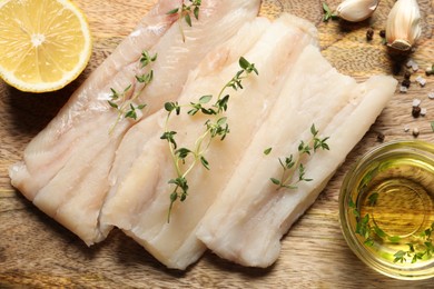 Photo of Raw cod fish, microgreens, lemon, oil and spices on wooden table, flat lay