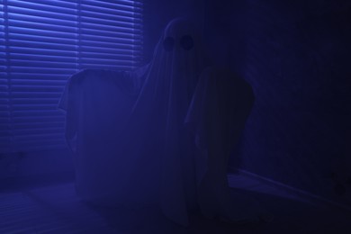 Photo of Creepy ghost. Woman covered with sheet near window in blue light