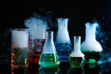 Photo of Laboratory glassware with colorful liquids and steam on black background. Chemical reaction