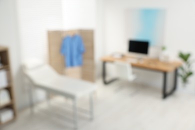 Photo of Blurred view of modern medical office with doctor's workplace and examination table in clinic