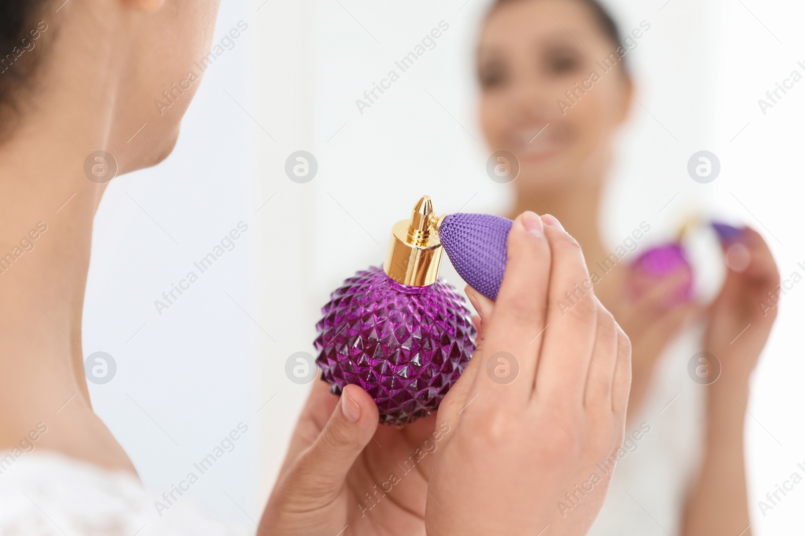 Photo of Young woman with bottle of perfume near mirror indoors