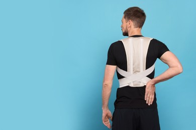 Man with orthopedic corset on blue background, back view. Space for text