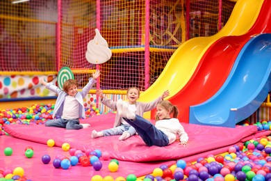 Happy kids playing in play room with slides, mats and ball pit