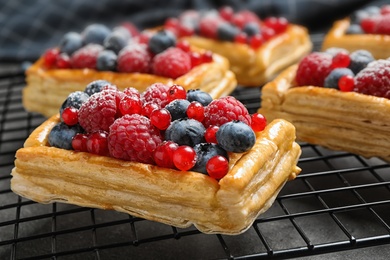 Cooling rack and fresh delicious puff pastry with sweet berries on grey table, closeup