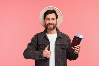 Smiling man with passport and tickets showing thumb up on pink background