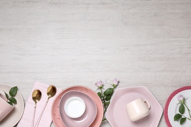 Flat lay composition with beautiful dishware and roses on white wooden table. Space for text