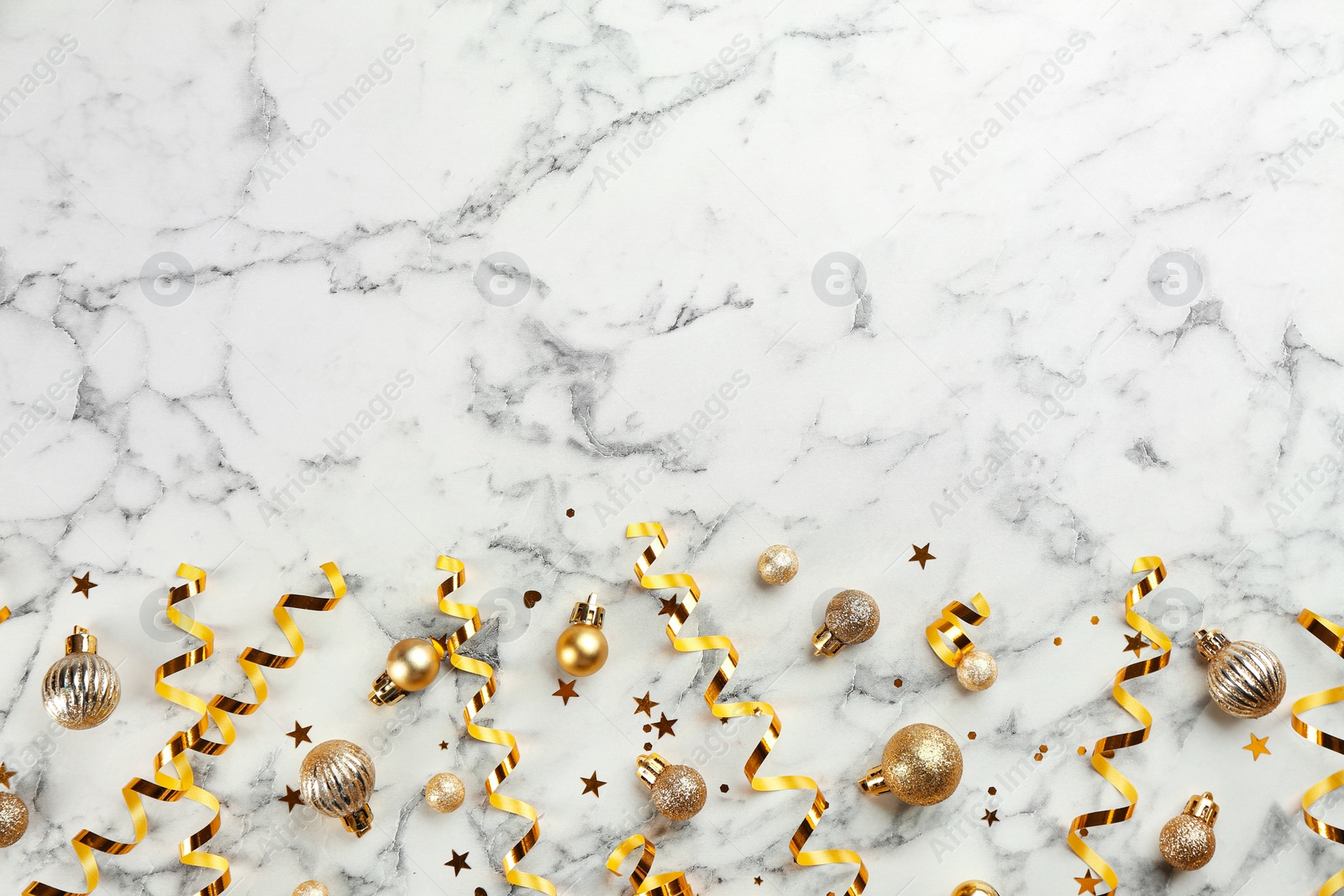 Photo of Shiny serpentine streamers and Christmas balls on white marble background, flat lay. Space for text