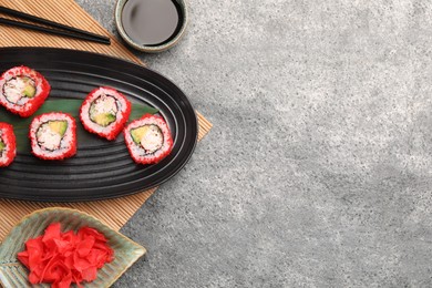 Photo of Delicious sushi rolls, soy sauce, ginger and chopsticks on grey textured table, flat lay. Space for text