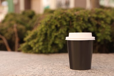 Photo of Takeaway paper cup with plastic lid on stone parapet outdoors, space for text