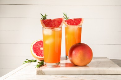 Tasty grapefruit drink with ice in glasses, rosemary and fresh fruits on light wooden table