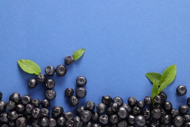 Photo of Ripe bilberries and leaves on blue background, flat lay. Space for text