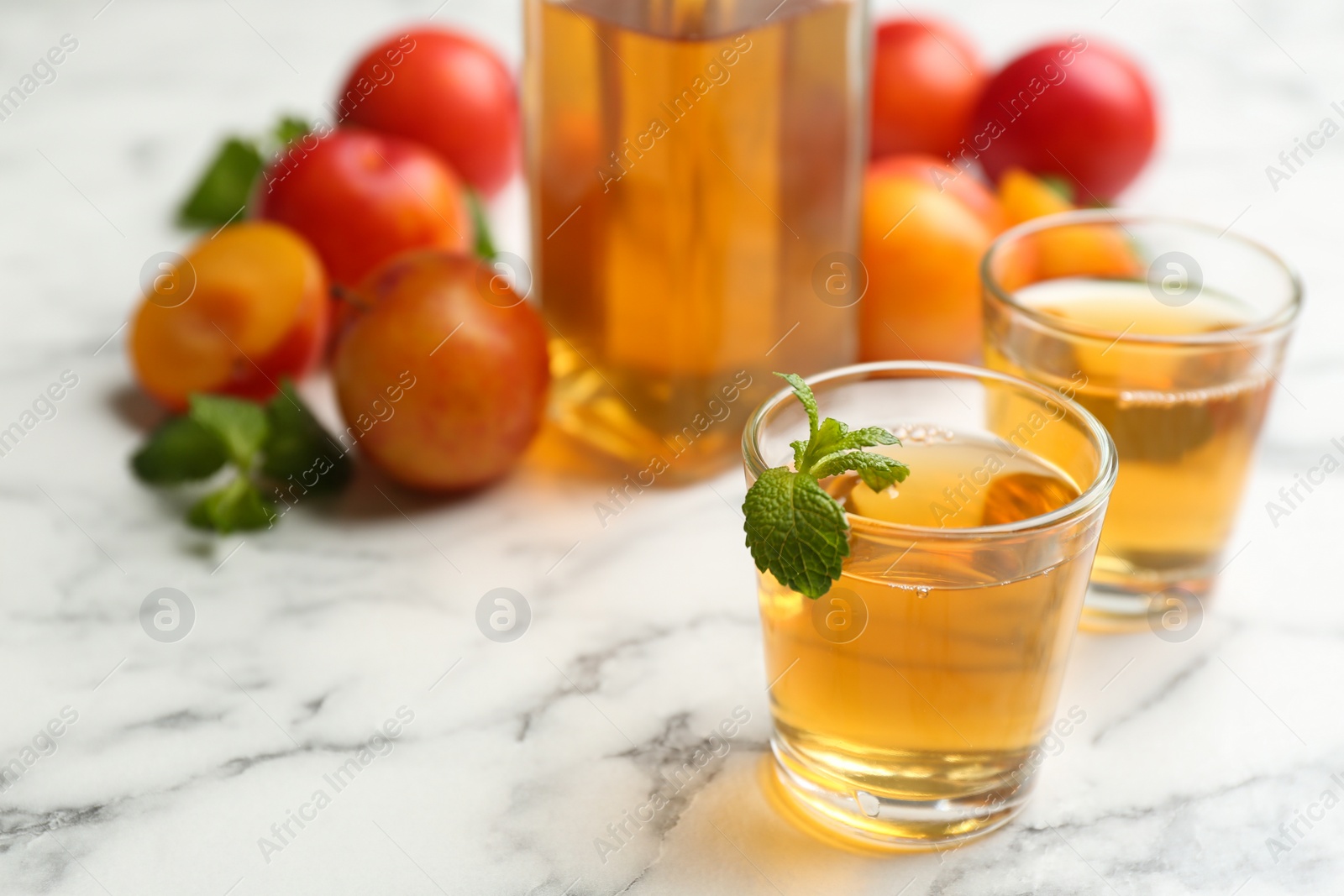 Photo of Delicious plum liquor with mint on white table. Homemade strong alcoholic beverage