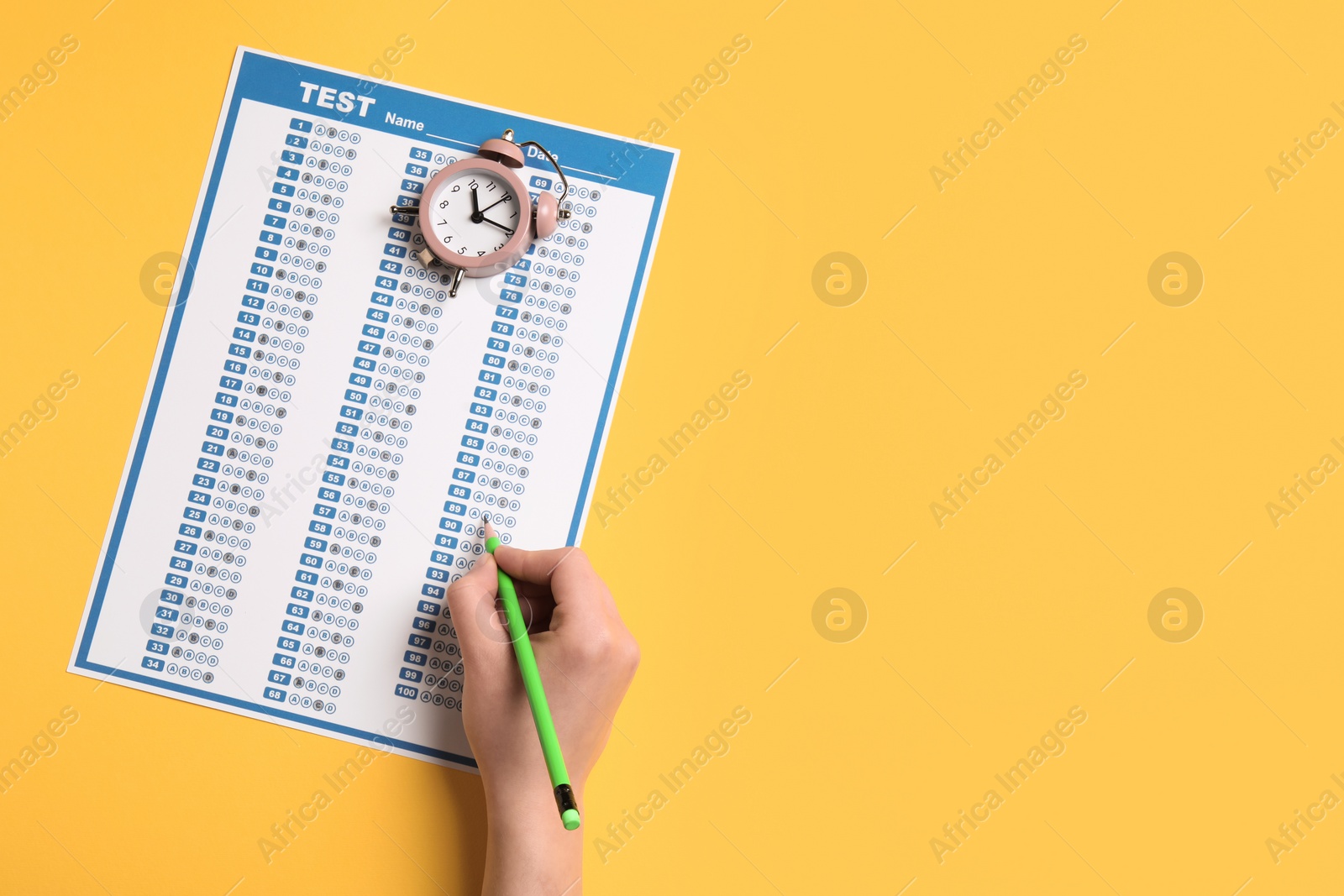 Photo of Student filling answer sheet on yellow background, top view with space for text. Passing exam