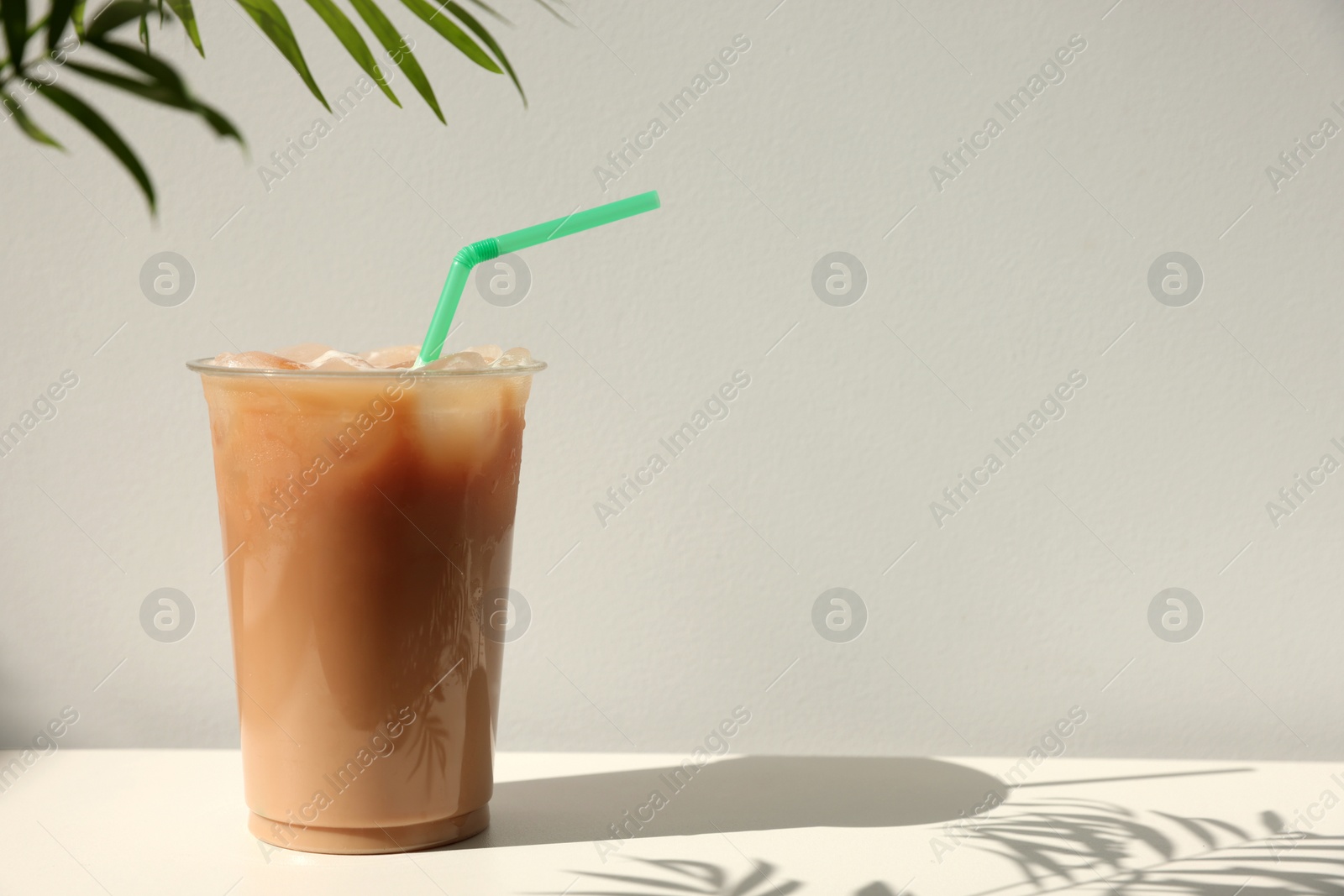 Photo of Plastic takeaway cup of delicious iced coffee on white table under sunlight, space for text