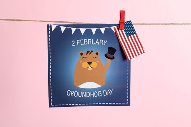 Photo of Happy Groundhog Day greeting card and American flag hanging on pink background