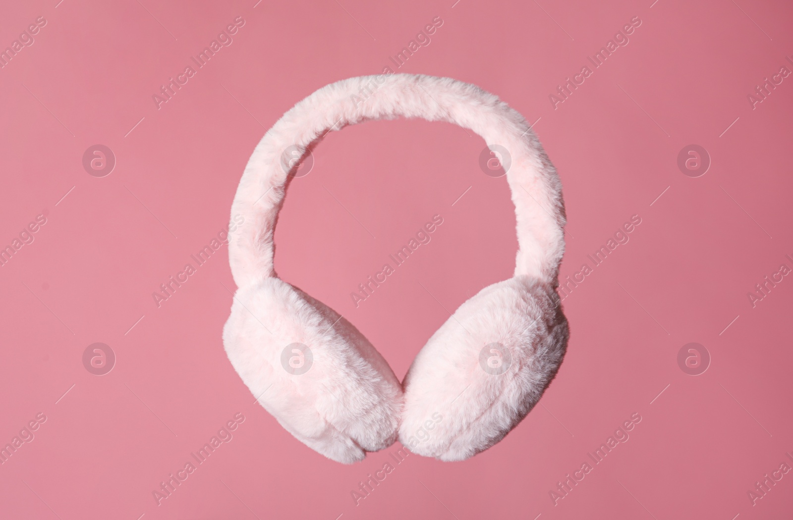 Photo of Fluffy earmuffs on pink background. Stylish winter accessory