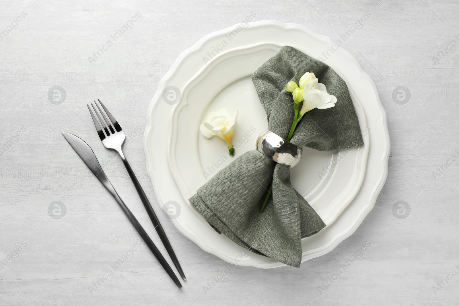 Photo of Stylish setting with cutlery, napkin, flowers and plates on light textured table, flat lay