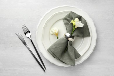 Photo of Stylish setting with cutlery, napkin, flowers and plates on light textured table, flat lay