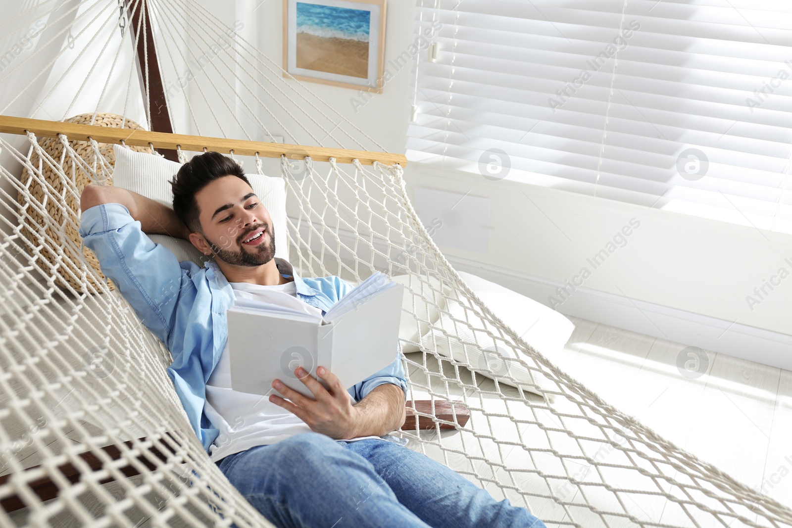 Photo of Young man reading book in hammock at home