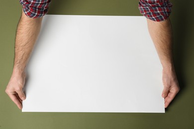 Man with empty sheet of paper on olive background, top view. Mockup for design