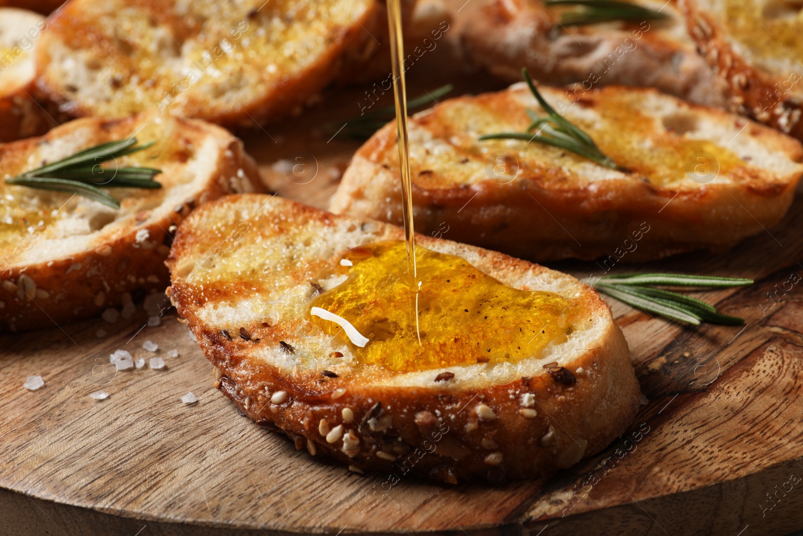 Photo of Pouring oil onto slice of toasted bread on wooden board, closeup