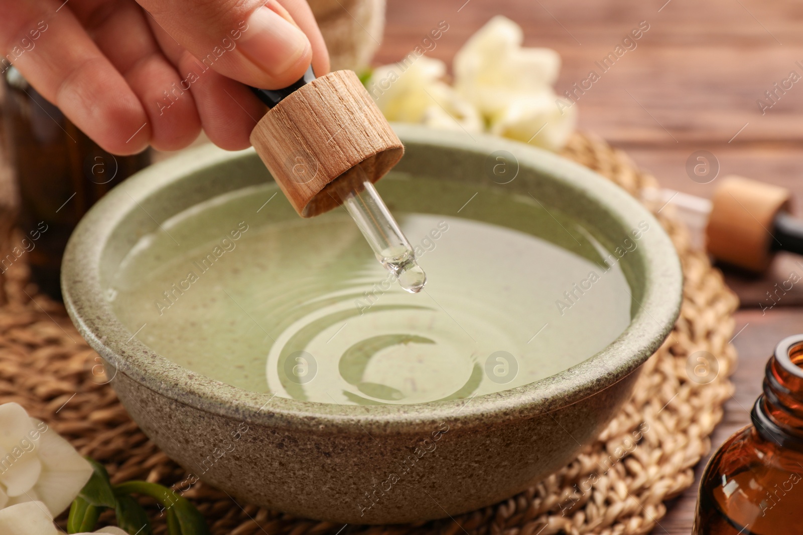 Photo of Woman dripping essential oil into bowl at wooden table, closeup. Aromatherapy treatment