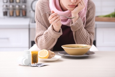 Photo of Sick young woman eating broth to cure cold at table in kitchen