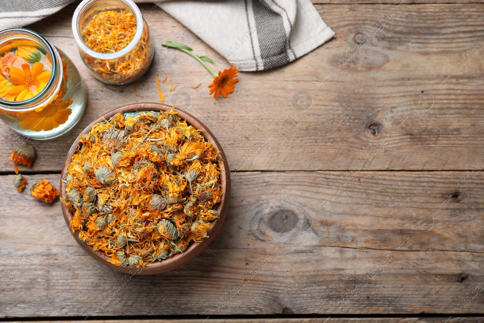 Photo of Bowl of dry calendula flowers and bottles with tincture on wooden table, flat lay. Space for text