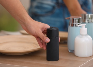 Photo of Young man taking deodorant from table in bathroom, closeup